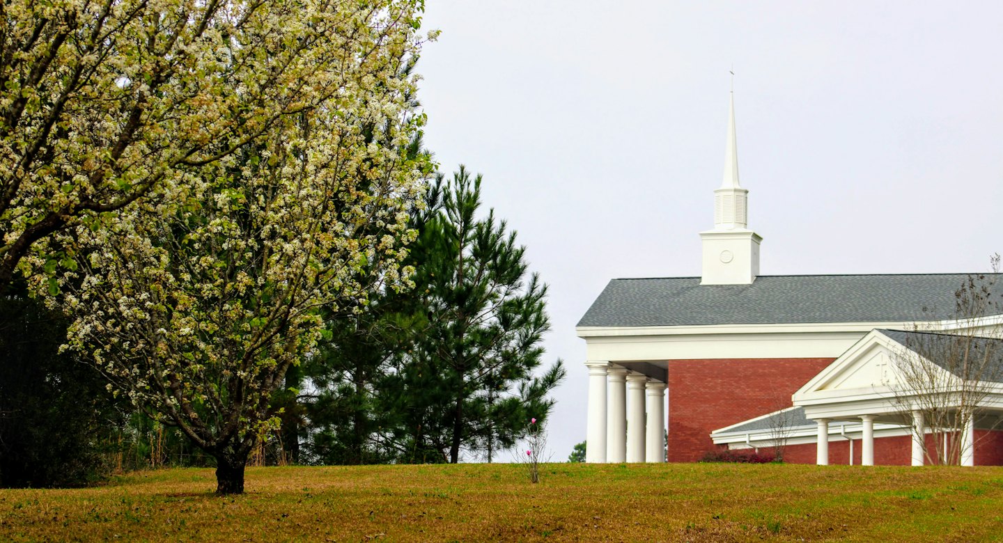 Modern red brick church with a white steeple on a hill.