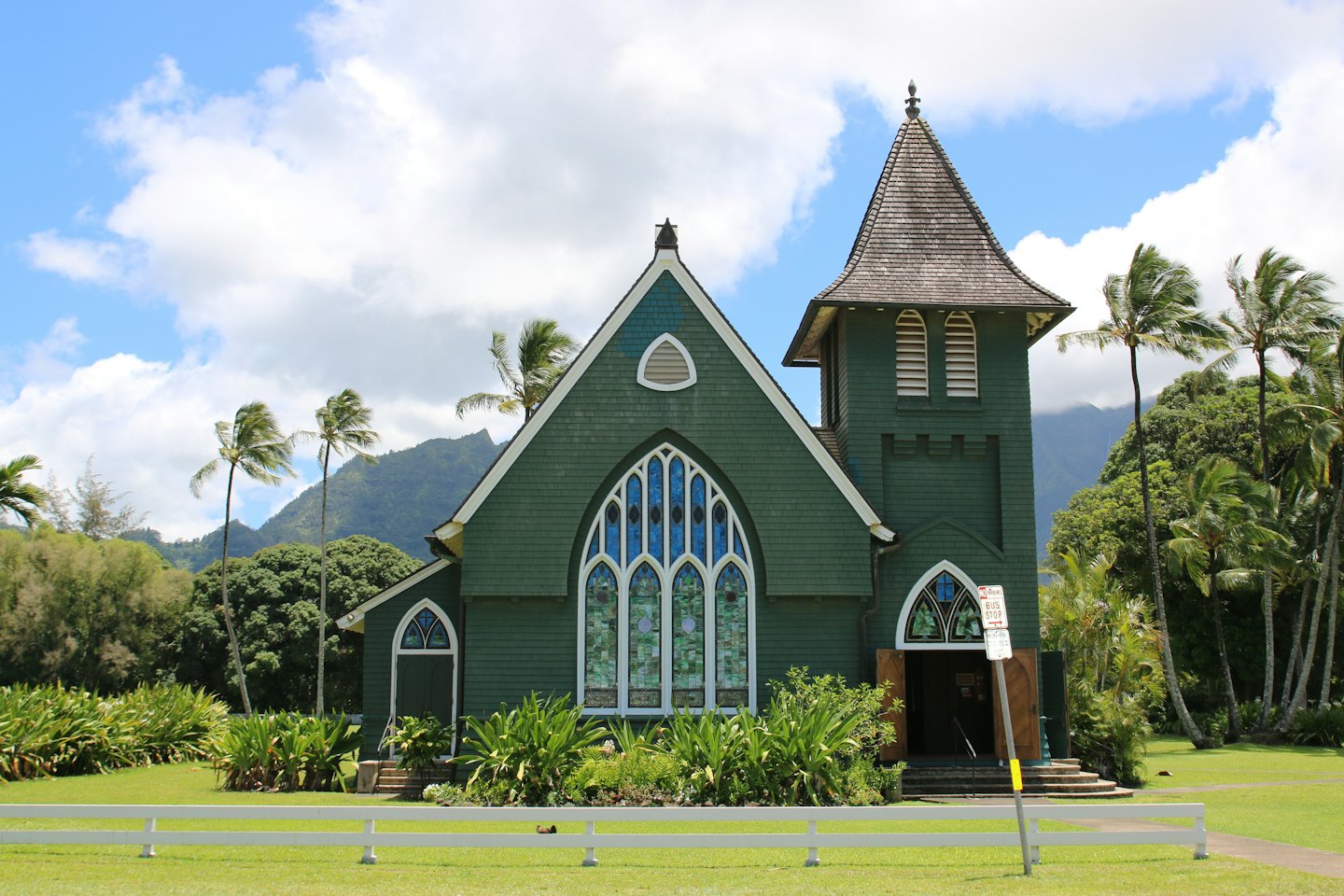 Green wooden church with a steeple stands behind a white fence.
